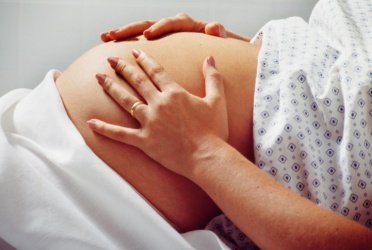 Pregnant woman in hospital gown rubs belly